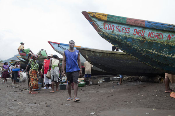 Foto van People walking past the fishing pirogues on the beach of LimbeLimbe - Kameroen