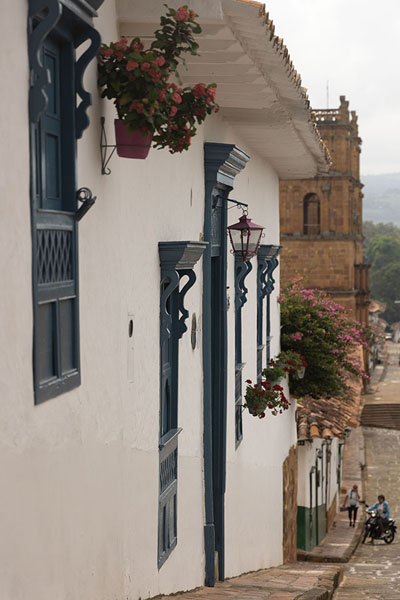 House with blue window shutters and bell tower of the cathedral of Barichara in the background | Barichara | Colombie