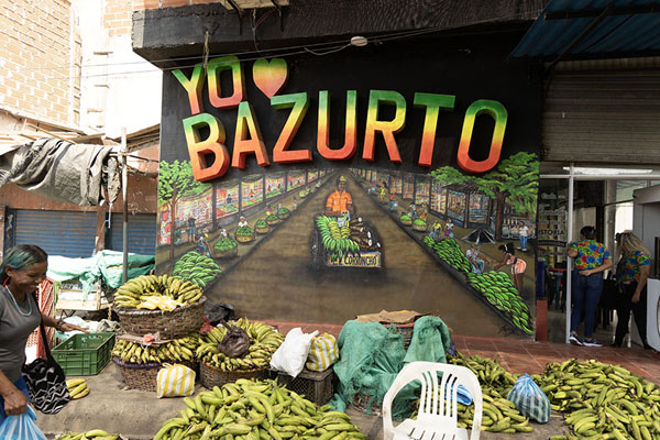 Smiling woman passing a painting of Bazurto market | Bazurto market | Colombie