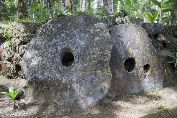 Stone money resting against the platform of Gilman; one of them with two holes | Gilman stone money bank | Federated States of Micronesia