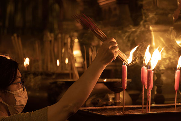 Picture of Woman lighting incense at one of the candles inside Man Mo TempleHong Kong - Hong Kong