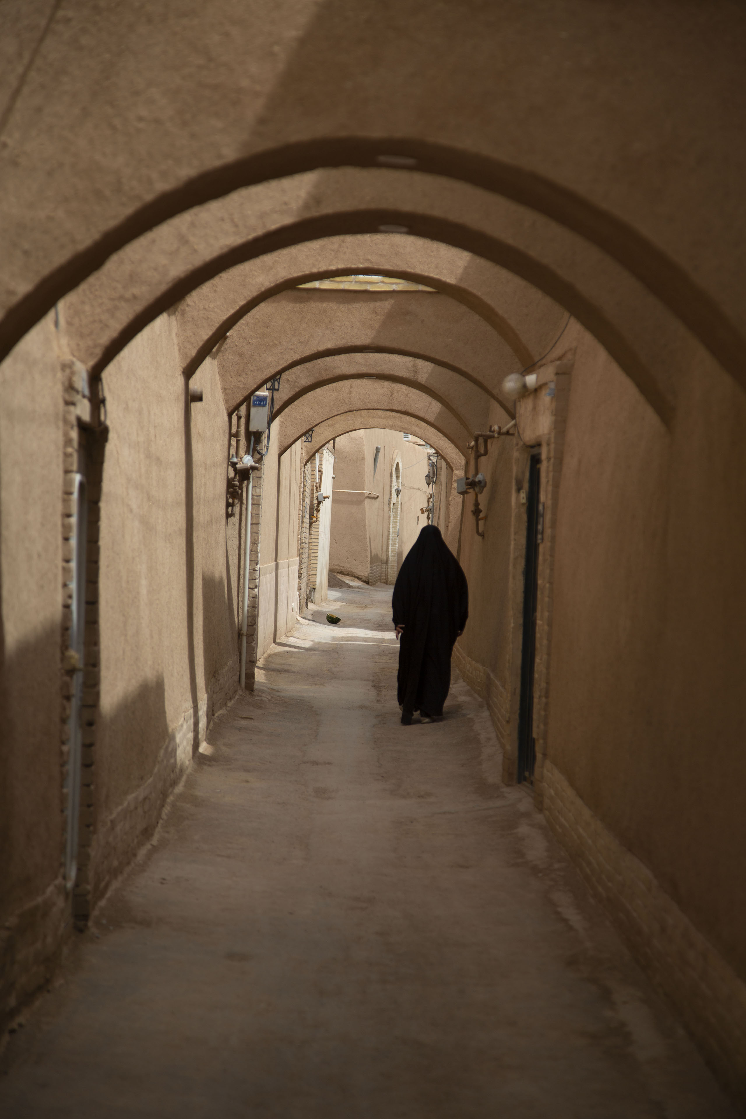 Woman walking a street with arches | Cité historique de Yazd | Iran