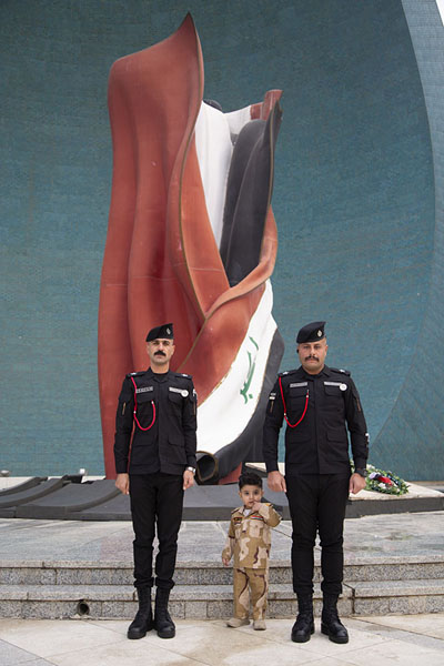 Picture of Two guards posing with a young boy at the Iraqi flagBaghdad - Iraq