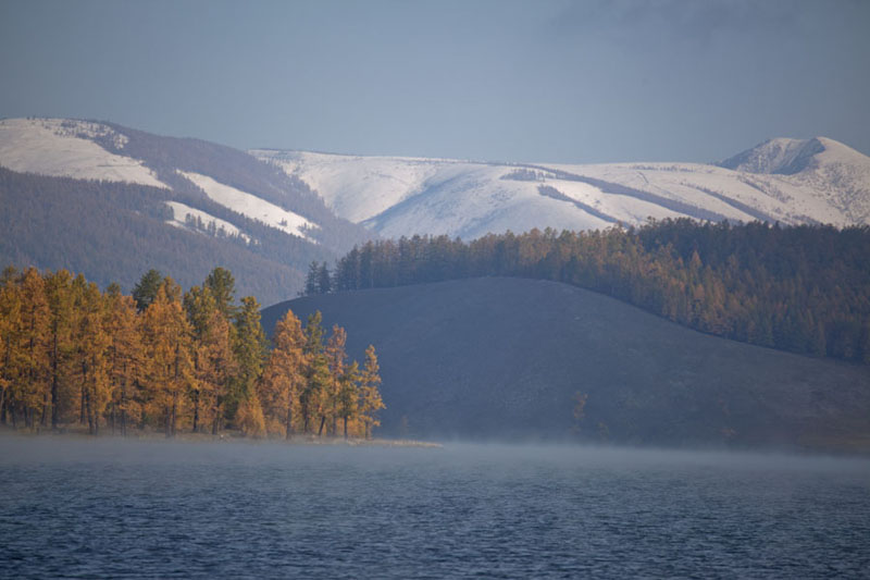 Looking across Khövsgöl Nuur with trees and snowy mountains in the background | Khövsgöl Nuur | Mongolia