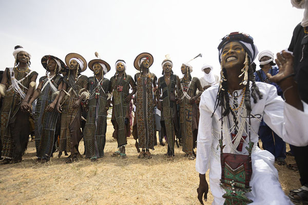 Foto van Wodaabe man on his knees with a line of other men behind him at the Gerewol festivalGerewol - Niger