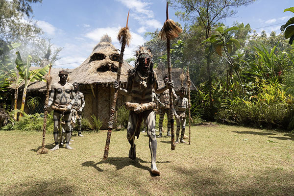 Foto van Asaro mudmen performing in front of a typical Asaro houseAsaro Mudmen - Papoea Nieuw Guinea