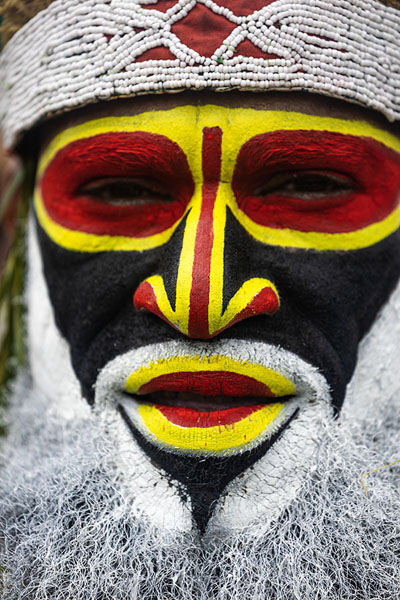 Foto van Man with face painted yellow, red, white and black at the Mount Hagen FestivalMount Hagen - Papoea Nieuw Guinea