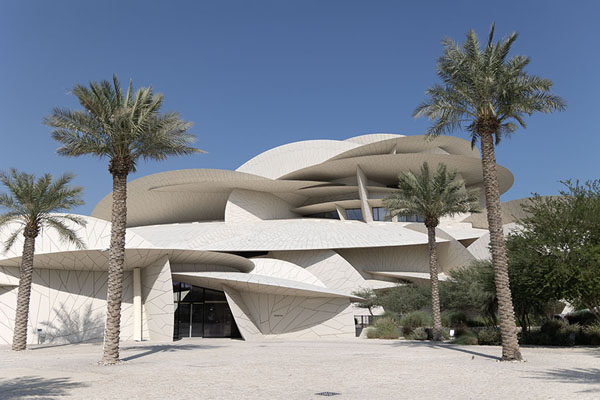 Palm trees with the clearly recognisable architecture of the desert rose in the background | National Museum Qatar | Qatar