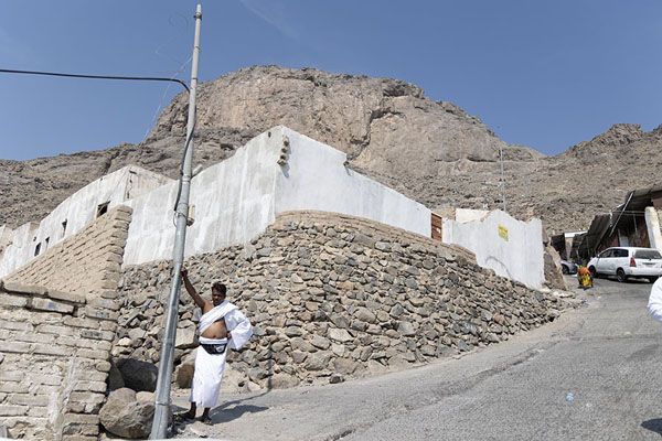 Foto van Man dressed in Umrah clothing resting against a pole with Jebel al Nour in the backgroundMekka - Saoedi Arabië