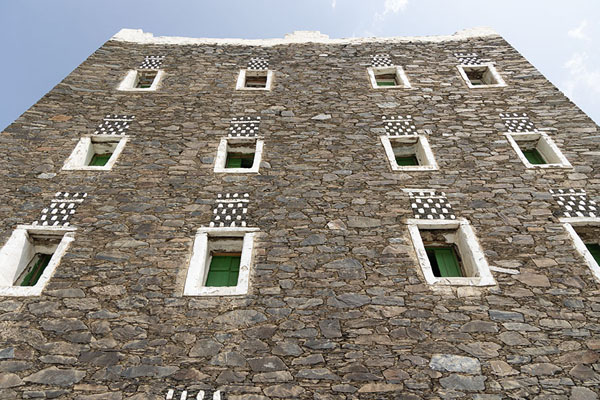 Looking up one of the tall buildings of Rijal Alma, with relatively small windows in the stone wall | Rijal Alma | Arabia Saudita