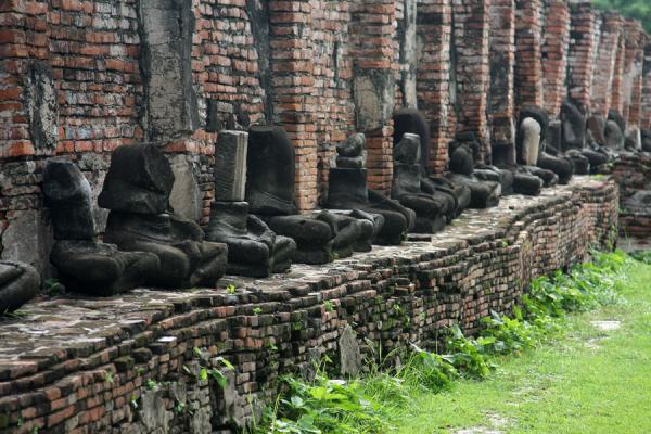 Row of headless Buddha statues sitting cross-legged against a wall | Wat Phra Mahathat | Thailand