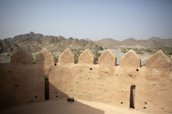 Crenellated wall on top of Wahla Fort with the countryside in the background | Fortezza Wahla | Emirati Arabi Uniti