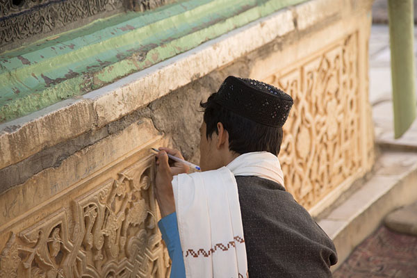 Man scribbling something on the marble at the base of the tomb of Ansari, Afghanistan