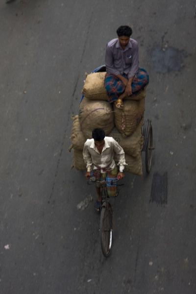 Man pedaling heavy load with a friend right on top, Bangladesh