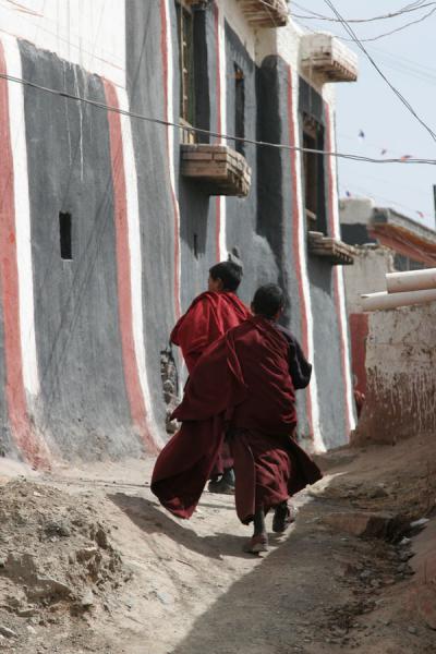 Two young monks running through an alley in Jyekundo Dondrubling | Monasterio Dondrubling | Cina