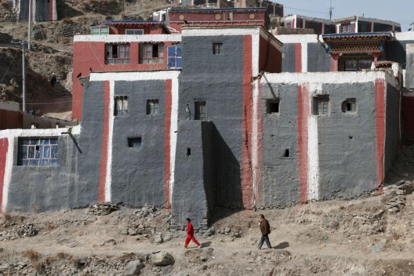People walking below one of the typically painted buildings of Jyekundo monastery | Monasterio Dondrubling | Cina