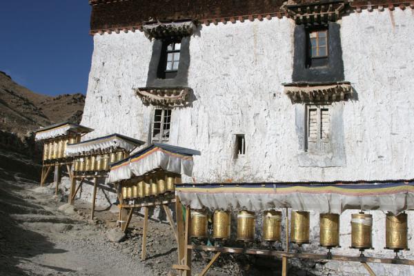 Typical Tibetan prayer wheels on Tashilhunpo kora, China Prayer wheels and building on the way up Tashilhunpo kora, China