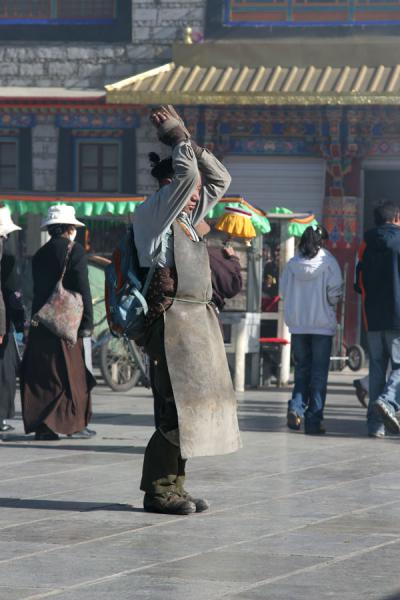 Devout Tibetan buddhist with protective cover prostrating in front of Jokhang temple | Pellegrini tibetani | Cina