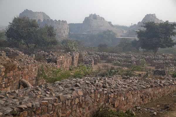 Crumbling wall with the defensive towers of Tughlaqabad Fort in the background, India