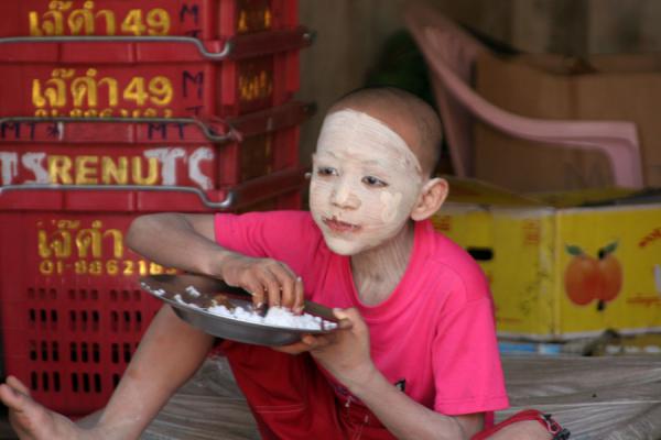 Young boy almost completely covered by tanakha having lunch, Myanmar