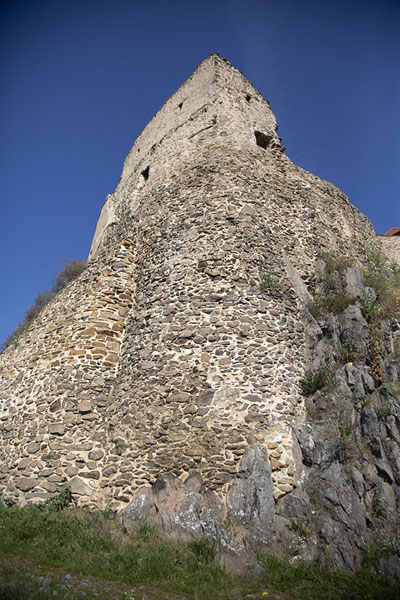 Looking up a rock with building on top | Alcázar de Rupea | Rumania
