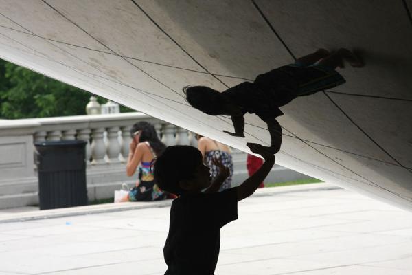 Boy playing with the distorted reflection of himself at the Bean, United States
